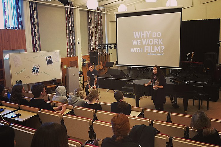 Workshop i musiksalen under Filmdagar på VBU 2020. Två lärare står framför en projektorduk med texten "Why do we work with film"?